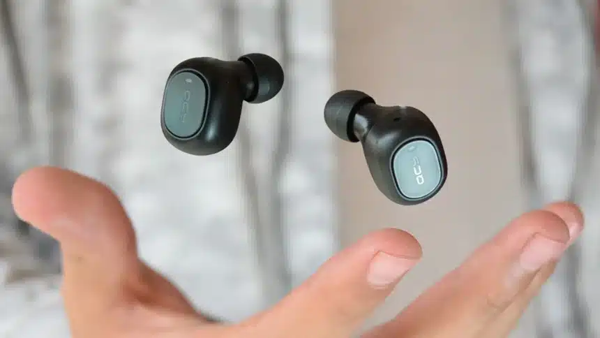 A pair of black QCY wireless earbuds featuring Environmental Noise Cancellation technology floating above an open hand